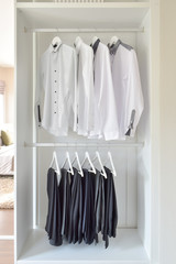 row of white shirts and black pants hanging  in wooden wardrobe