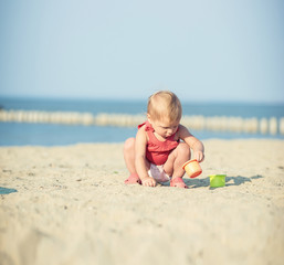Baby playing on the sandy beach near the sea. Cute little girl in red dress with sand on tropical beach. Ocean coast.