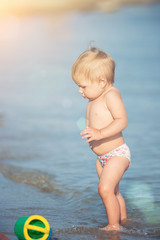 Baby playing on the sandy beach and in sea water. Cute little kid with toys on sand tropical beach. Ocean coast.