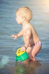 Baby playing on the sandy beach and in sea water. Cute little kid with toys on sand tropical beach. Ocean coast.