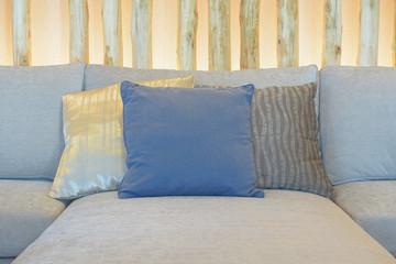 Blue pillow setting on light gray sofa with decorative wooden in background