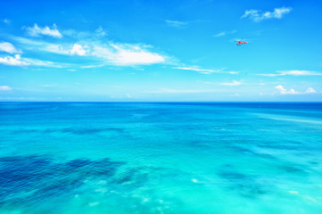 Small red helicopter in blue sky blue ocean horizon