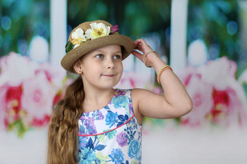 Cute long haired girl adjusts flowers decorated hat on her head - children beauty and fashion concept