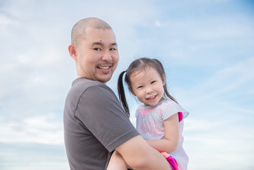 Asian father holding his daughter over sky background
