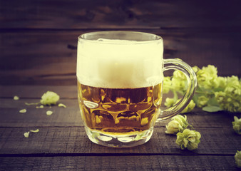 Draft cold beer in glass jar with green ripe hop cones on black