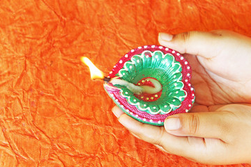 decorative diya in hand on bright orange texture background for Diwali cards and wishes