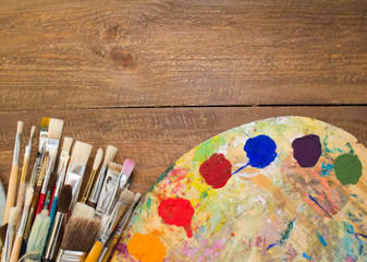 Paints, brushes and palette on the colorful background. The workplace of the artist. Banner for...