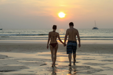 Silhouette of couple walking on beach at sunset holding hands. Horizontally framed shot.