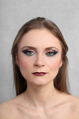 Pretty young woman with bright evening makeup on serious face close up on gray background