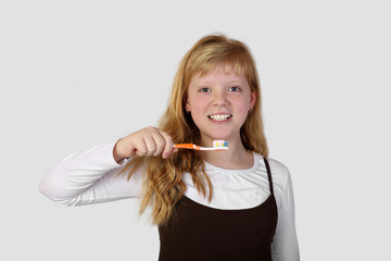 Teenage blonde girl with a toothbrush in hand going to brush teeth on gray background