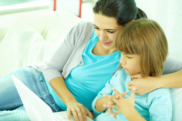 Young mother with her daughter watching something on laptop