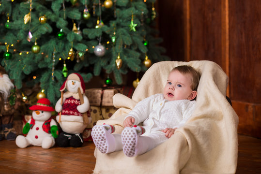 A baby in white knitted woolen costume holds gift box