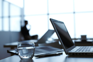 Laptop, pen and glass of water on the table with businessman working on background