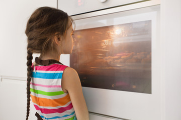 Fototapeta na wymiar Little girl waiting near the kitchen oven for homemade cookies