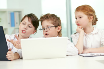 Fototapeta na wymiar Three little business children discussing something at computer