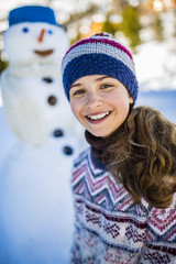 Happy smiling teenage girl playing with a snowman on a snowy win