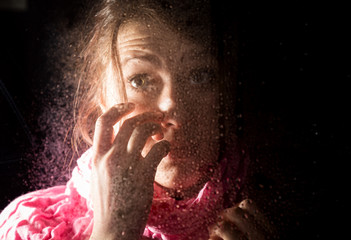 young sad woman portrait behind the window in the rain with rain drops on it