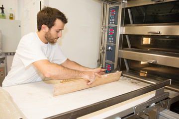 Male baker baking fresh bread in the bakehouse near oven