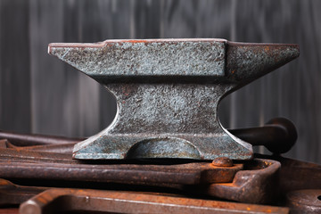 Old rusty rugged anvil on top of other blacksmith tools.