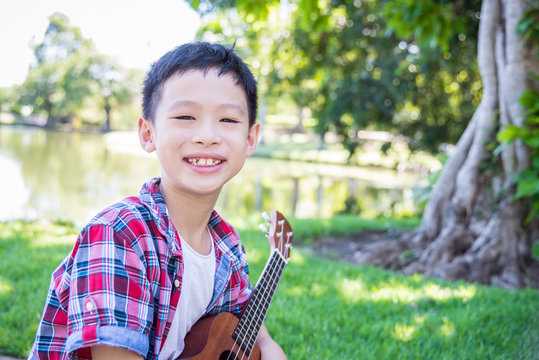 Young asian boy playing ukulele in park