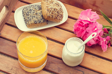 Fototapeta na wymiar Bandeja de madera con Vaso de zumo de naranja, yogur y panes al aire libre. Vista superior