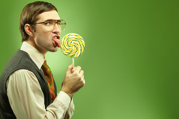 Portrait of nerd boy sucking a lollipop and looking at camera in suspense  - obrazy, fototapety, plakaty