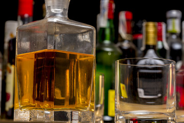 Close-up of whisky bottle beside an empty glass, in front of different alcoholic drink bottles
