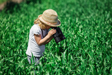 Naklejka na ściany i meble Little girl in the field looking away through the binoculars