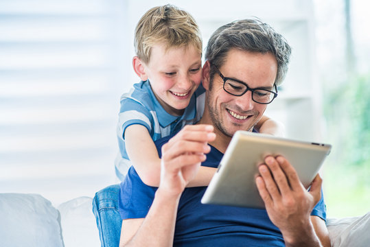 A Father And His Young Son Having Fun By  Playing On A Tablet