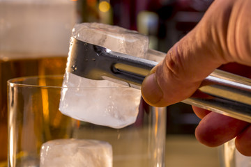 Adding an ice cube into the glass with the tongs. Serving a whisky on the rocks