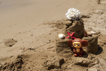 Sandcastle with starfish, coral and toy on sandy beach