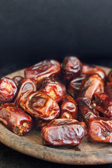 Dried dates fruit in rustic plate on black background. Copy space