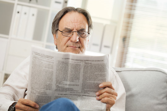 Senior man reading newspaper in home