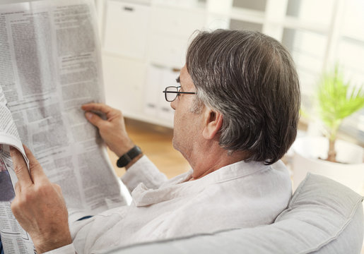 Senior man reading newspaper in home