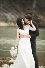 Beautifull wedding couple kissing and embracing near the shore of a mountain river with stones