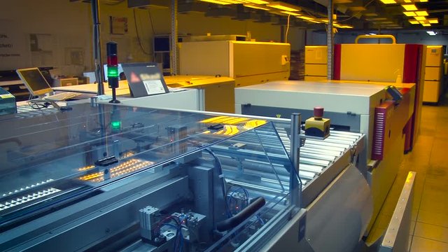 Print Shop. Process Line. Digital Equipment. Piece of Paper Moving on Conveyer, Getting Into Glass Box With Turning Mechanism. Electric Yellow Light