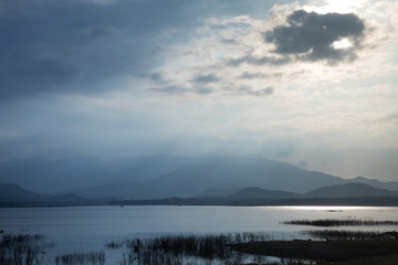 Obraz premium Rays of sun shining through the clouds and sunset over water