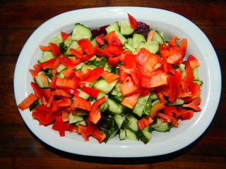 In a white bowl on a wooden board chopped peppers, cucumber, red beet. Vegetarian salad.