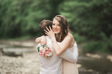 Beautifull wedding couple kissing and embracing near the shore of a mountain river with stones