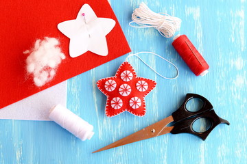 Felt Christmas star diy, paper pattern pinned to red felt sheet, scissors, thread, needle, cord on blue wooden background. Christmas background. Winter sewing diy for children and beginners