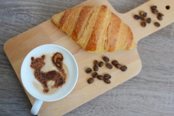 cup of cappuccino and yummy croissant on wooden table