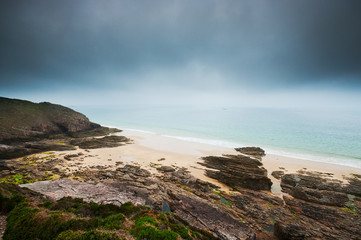 Beach with rocks and cloudy dark sky in Cap Frehel, Brittany, France