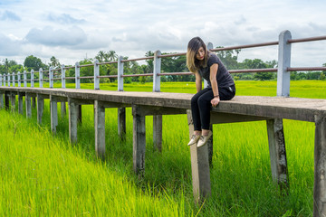 Asian woman sitting on elevated pathway in rice field