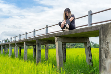 Thai woman sitting on elevated walkway in rice field