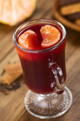 Heißer Glühwein mit Mandarinenspalten in Glas serviert (Selektiver Fokus, Fokus auf den Vorderteil des rechten Mandarinstückchens)