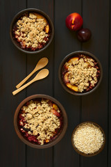 Englische Frucht Crumble oder Crisp, eine gebackene Süßspeise aus Obst (hier: Pflaume und Nektarine) und Haferflocken Streusel, fotografiert auf dunklem Holz mit natürlichem Licht