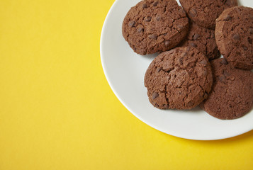 A plate of chocolate chunk cookies on a bright yellow background forming a page border