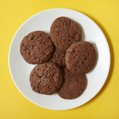 A plate of chocolate chunk cookies on a bright yellow background