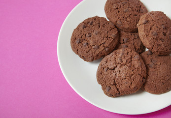 A plate of chocolate chunk cookies on a bright pink background forming a page border