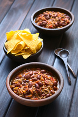 Chili con Carne aus Kidney-Bohnen, Hackfleisch, Tomaten und Zwiebeln mit Tortilla Chips an der Seite, fotografiert mit natürlichem Licht (Selektiver Fokus, Fokus in die Mitte des ersten Chilis)